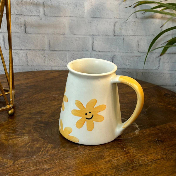White mug with yellow flower designs on a wooden table against a stone wall.