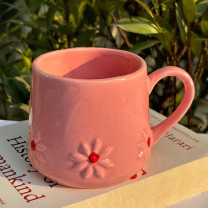 Pink mug with floral design on a book with green leaves in the background