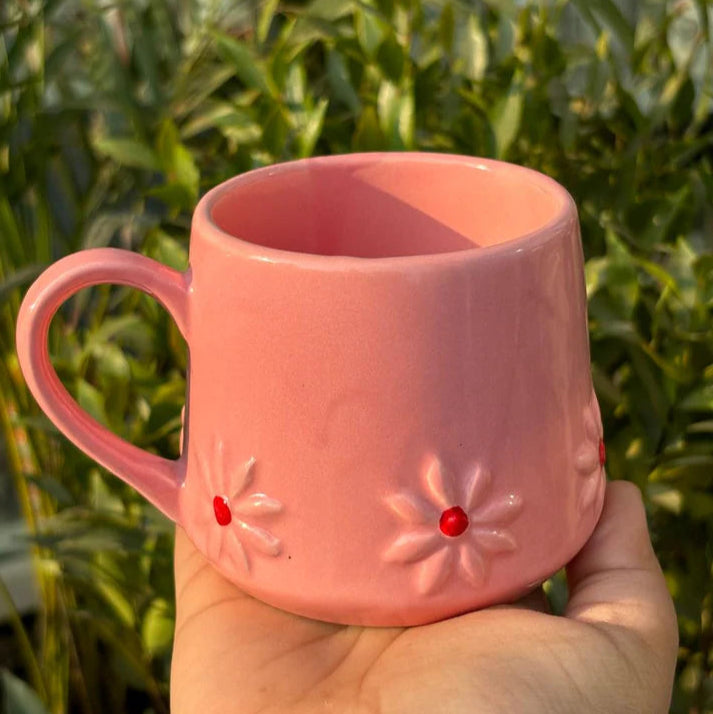 Pink mug with floral designs held in a hand against a green leafy background