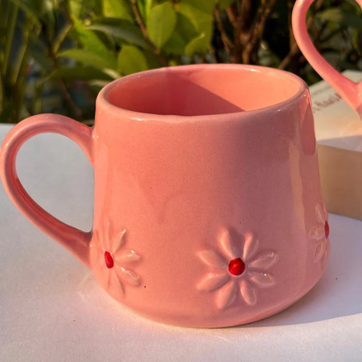 Pink mug with floral designs on a white surface with greenery in the background