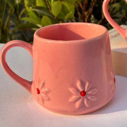 Pink mug with floral designs on a white surface with greenery in the background