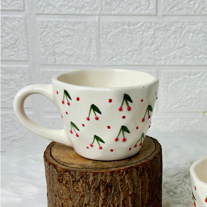 Two ceramic mugs with cherry design on a wooden block against a white tiled wall.