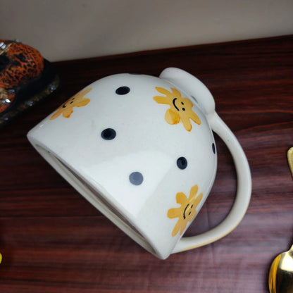 White mug with black polka dots and yellow smiley faces on a wooden surface
