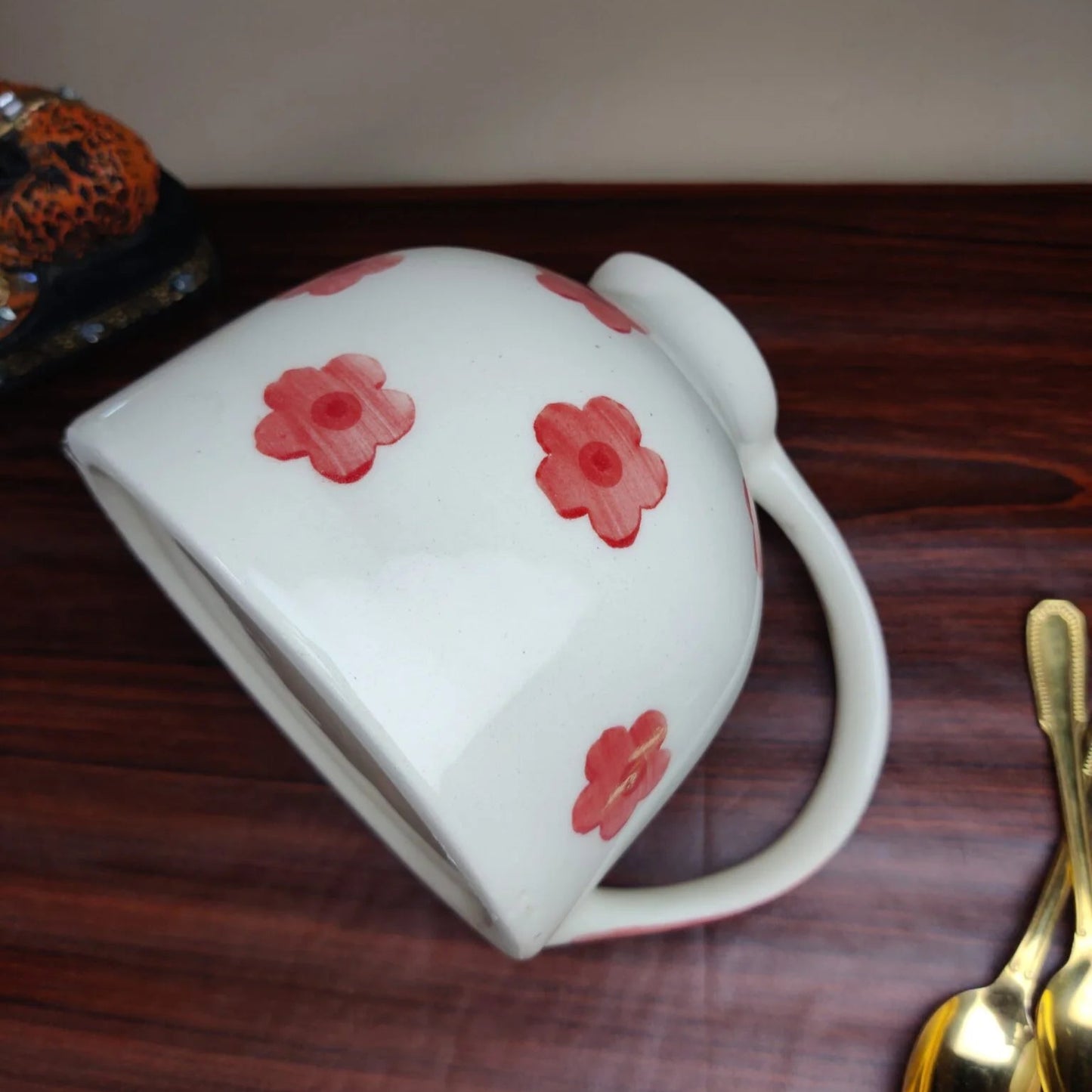 White mug with red floral patterns on a wooden surface with gold spoons.