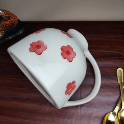 White mug with red floral patterns on a wooden surface with gold spoons.