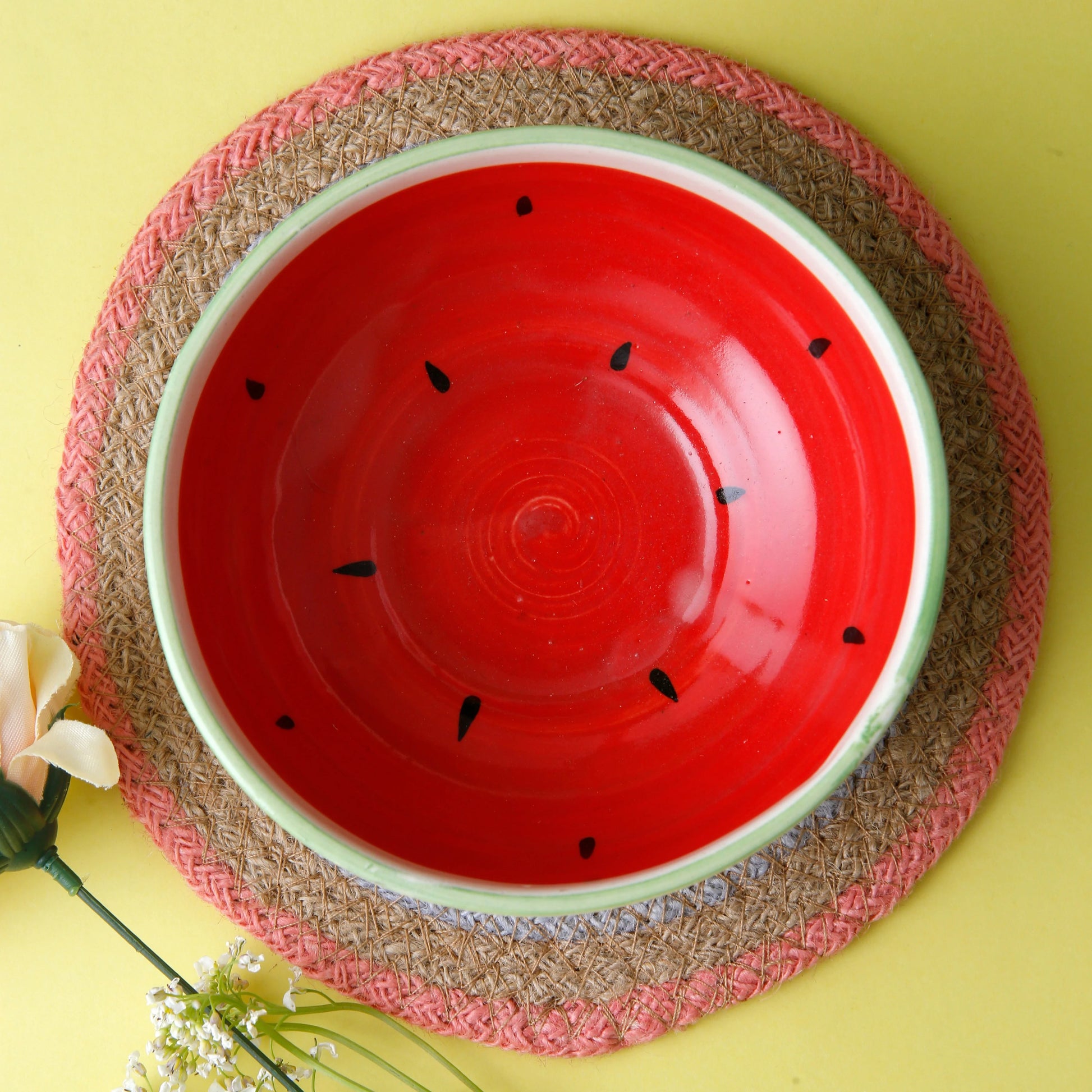 Red ceramic bowl with watermelon design on a woven placemat against a yellow background