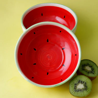 Two red ceramic bowls with watermelon design on a yellow background, accompanied by kiwi slices.