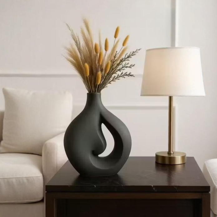 Decorative vase with dried plants on a table next to a lamp and sofa.