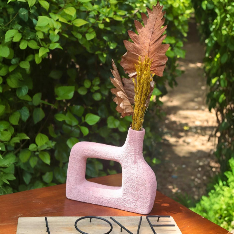 Pink textured vase with dried leaves on a wooden surface outdoors