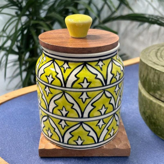 Ceramic jar with yellow and white pattern and wooden lid on a blue surface.