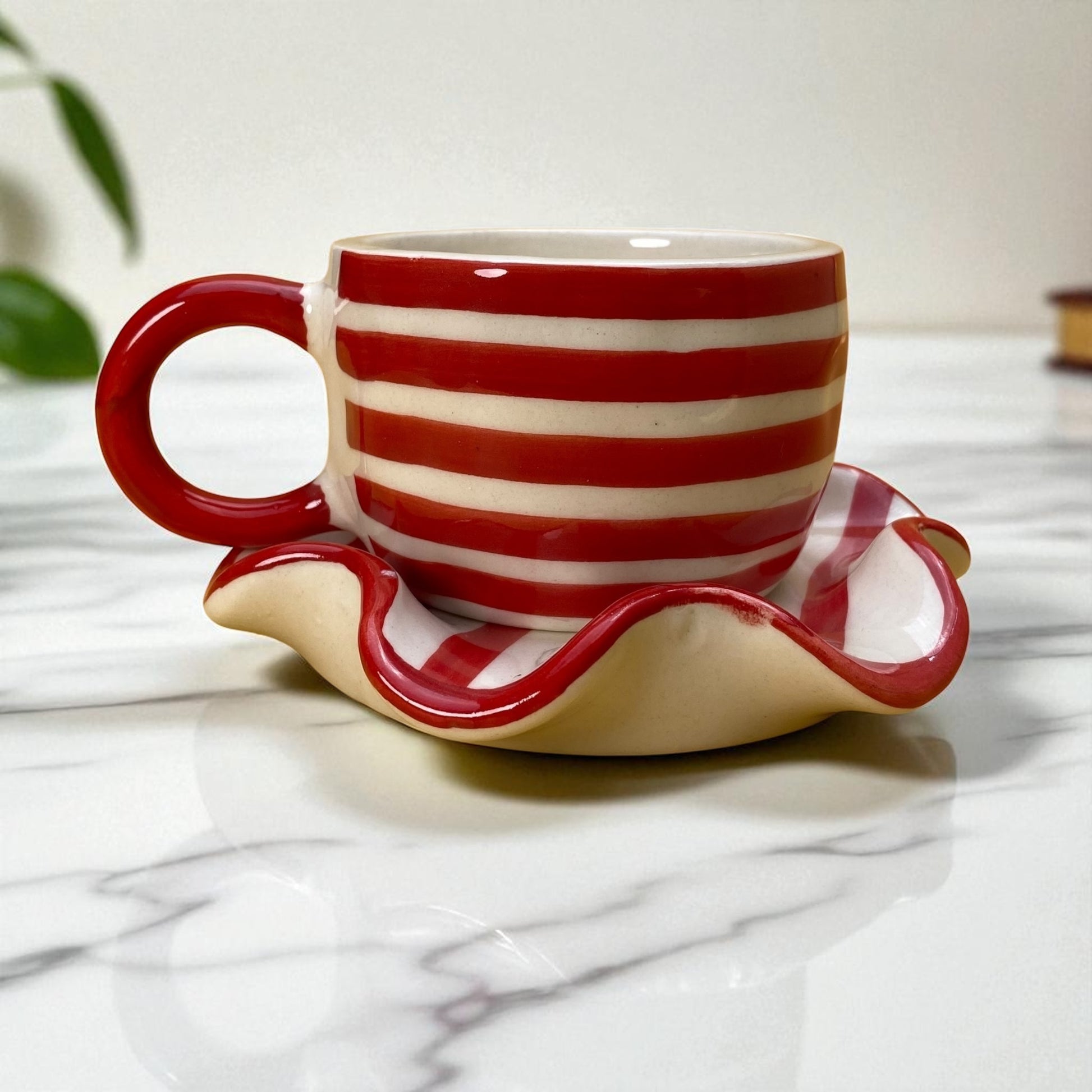 Red and white striped ceramic cup and saucer on a marble surface