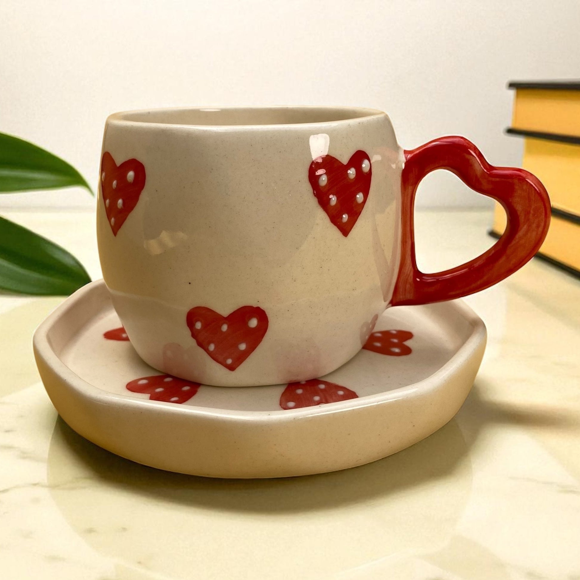 Ceramic cup with red heart designs on a matching saucer, placed on a marble surface.