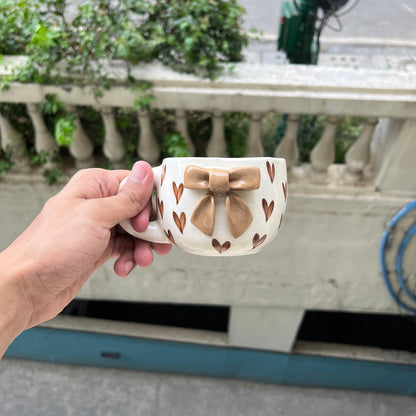 Hand holding a decorative mug with bow design outdoors