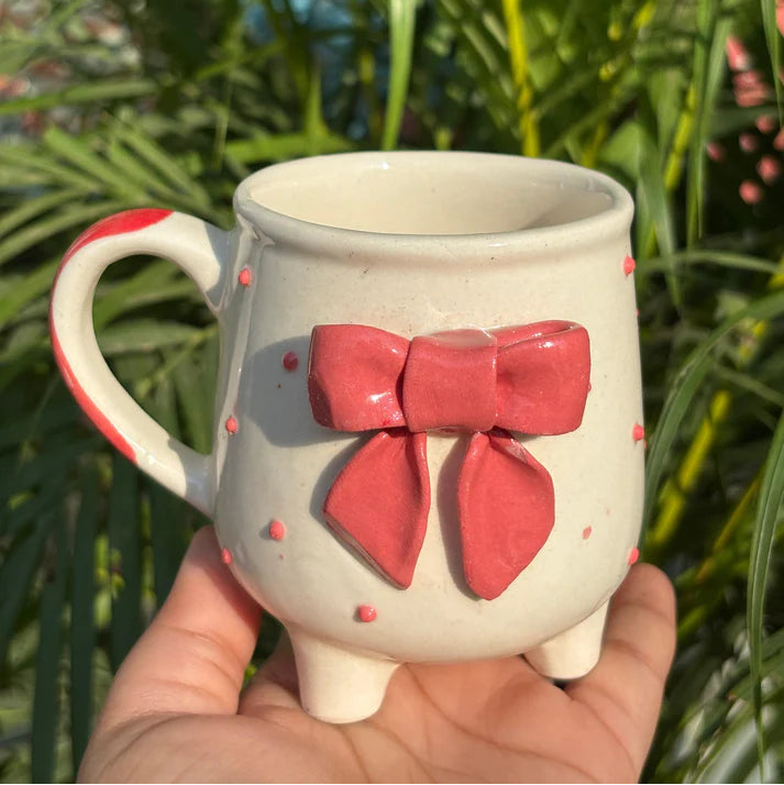 Ceramic mug with a red bow design held in front of green foliage