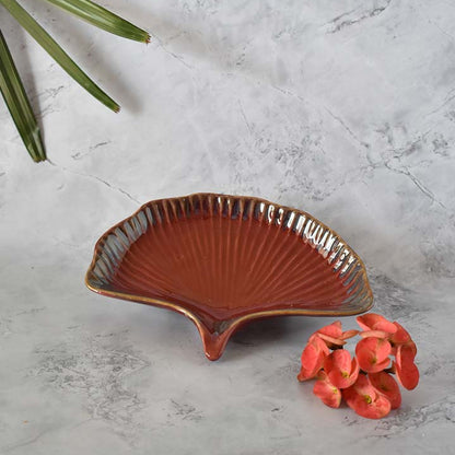 Ceramic fan-shaped dish on a marble surface with a small plant and pink flowers.