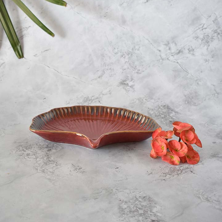 Brown ceramic dish on a textured gray surface with red flowers and green leaves.