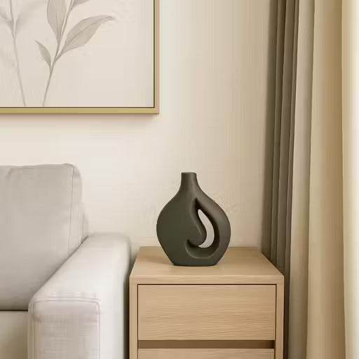 Decorative vase on a wooden side table next to a gray sofa with a light-colored wall and framed artwork in the background.